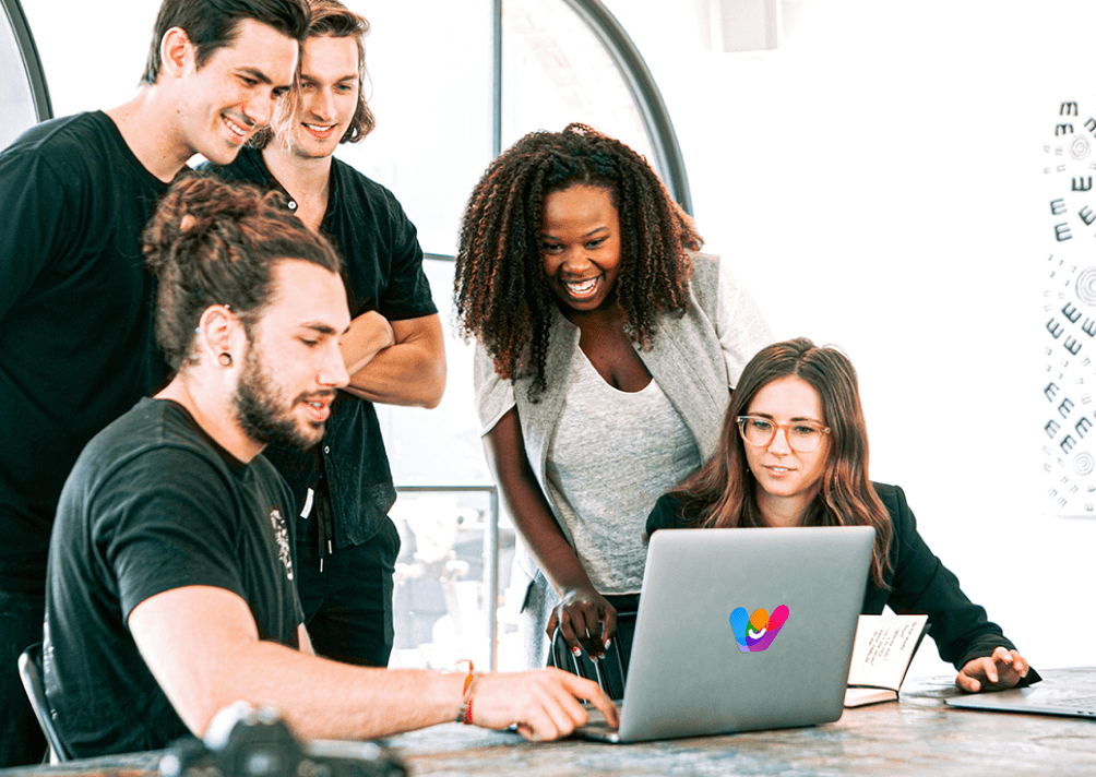 Un gruppo eterogeneo di cinque giovani professionisti che lavorano insieme attorno a un laptop in un ambiente d'ufficio luminoso con il logo di Wishraiser sul laptop